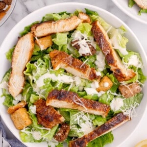 Prepared caesar salad with parmesan cheese and seasoned chicken on top.