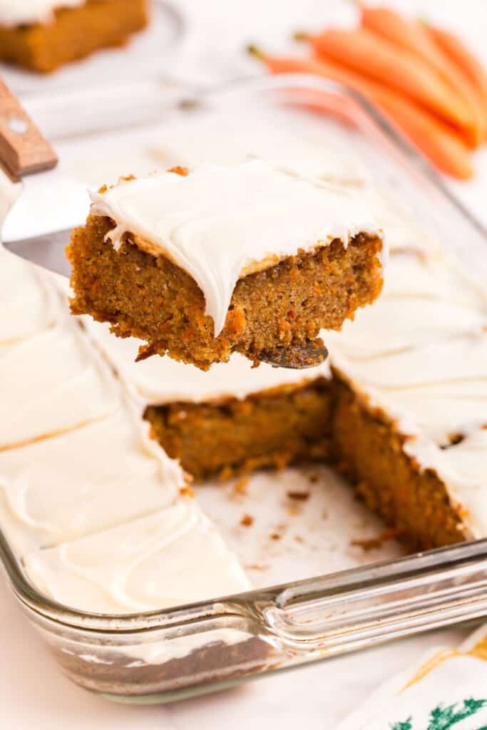 A serving of carrot cake lifted above the baking pan of carrot cake.