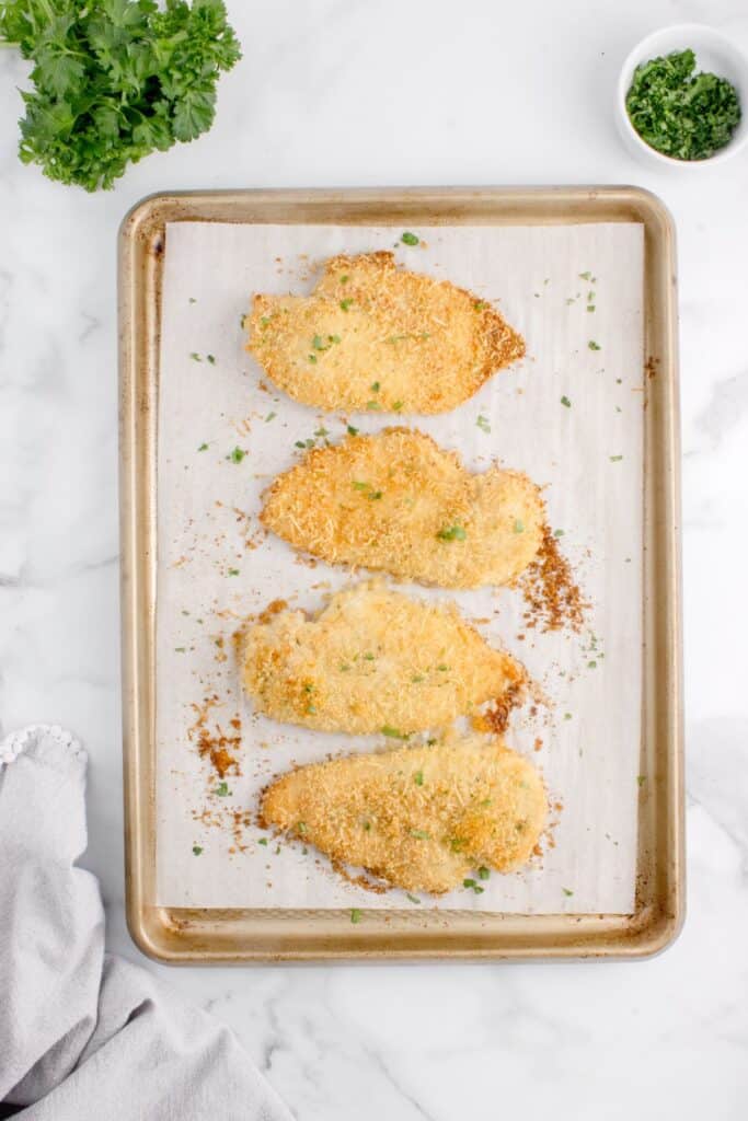 Four pieces of parmesan crusted chicken on a parchment lined baking sheet.