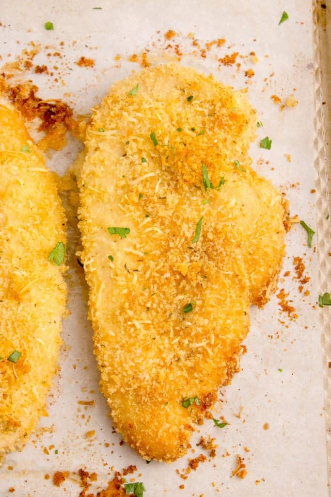 Baked parmesan crusted chicken on a parchment lined baking sheet.