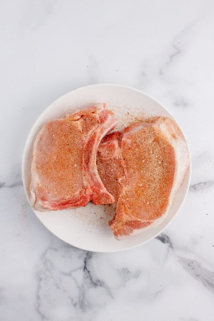 Raw, seasoned pork chops on a white plate.