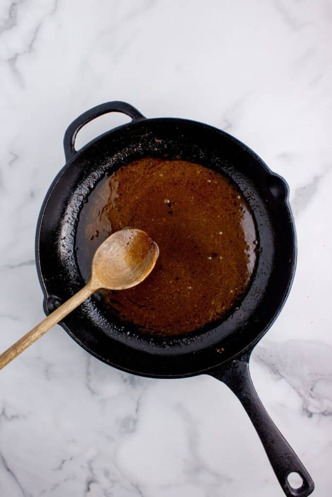Cast iron pan with brown sugar glaze. A wooden spoon is stirring the glaze.
