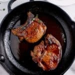 Cast iron pan with cooked pork chops and a sprinkle of parsley.