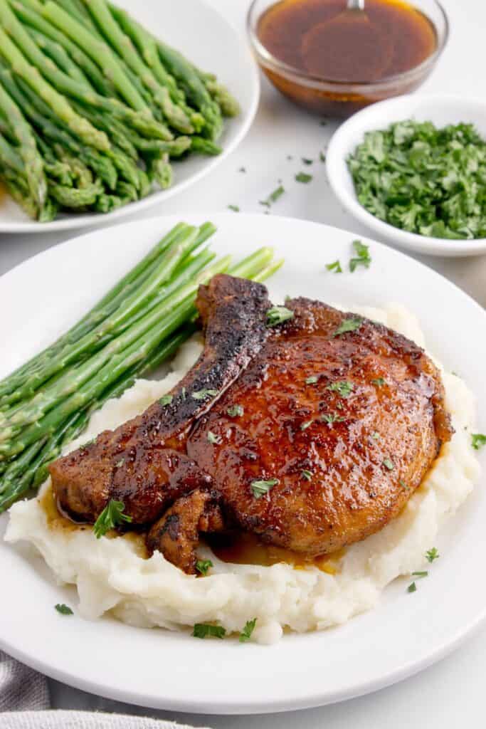 White dinner plate with a pork chop over mashed potatoes and asparagus spears.