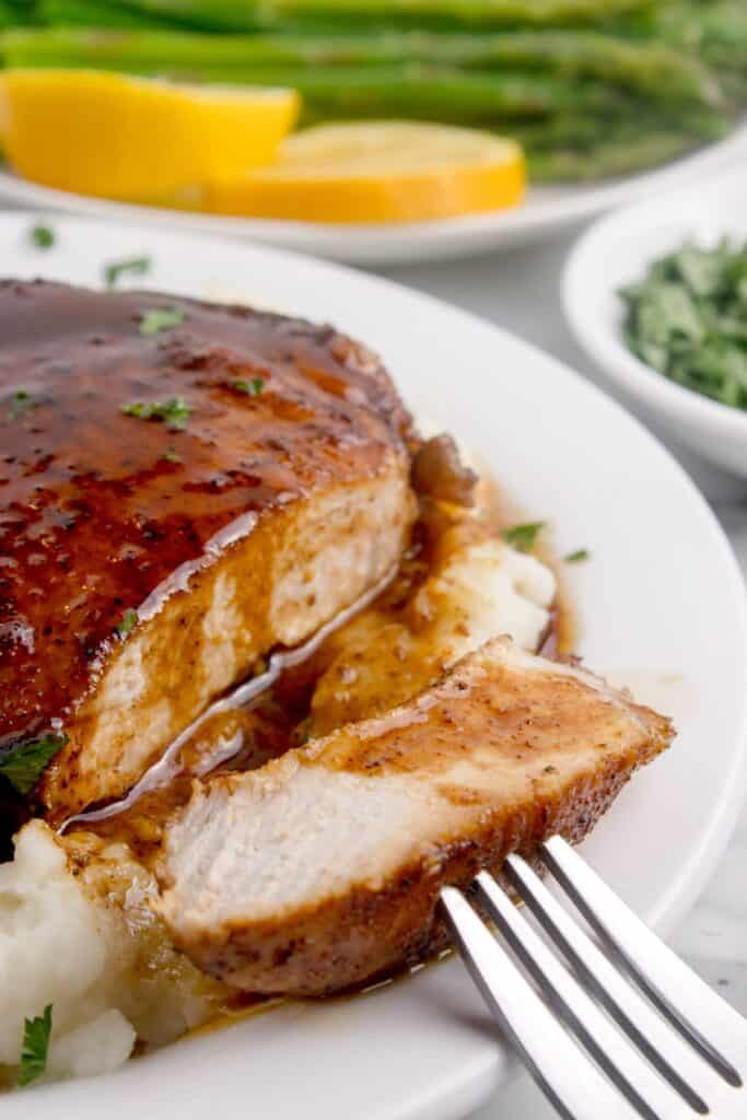 Sliced pork chop on a dinner plate. A fork is removing a bite to show the interior of the pork chop.