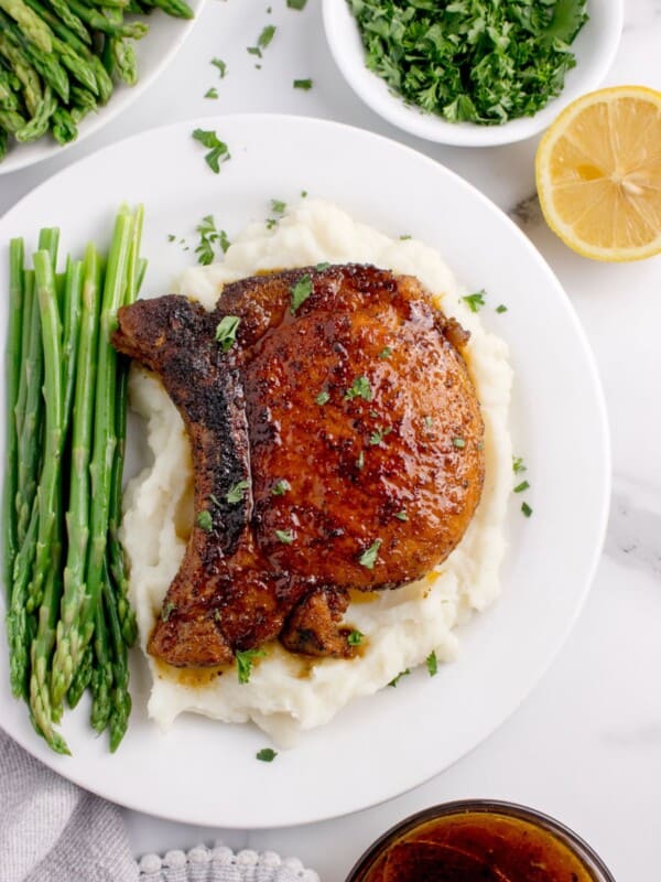 White dinner plate with a pork chop over mashed potatoes and asparagus spears.
