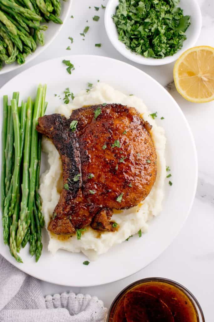 White dinner plate with a pork chop over mashed potatoes and asparagus spears.