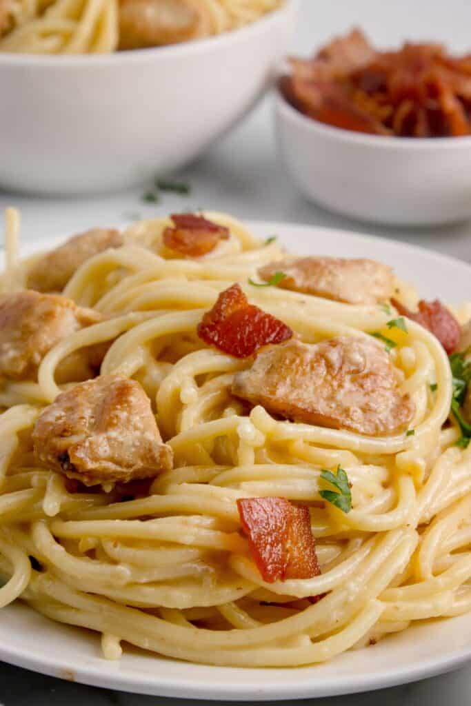 A white dinner plate with a serving of chicken carbonara on it.