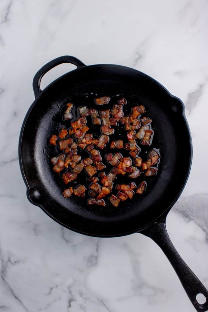 Cast iron pan with cooked bacon bits in it.