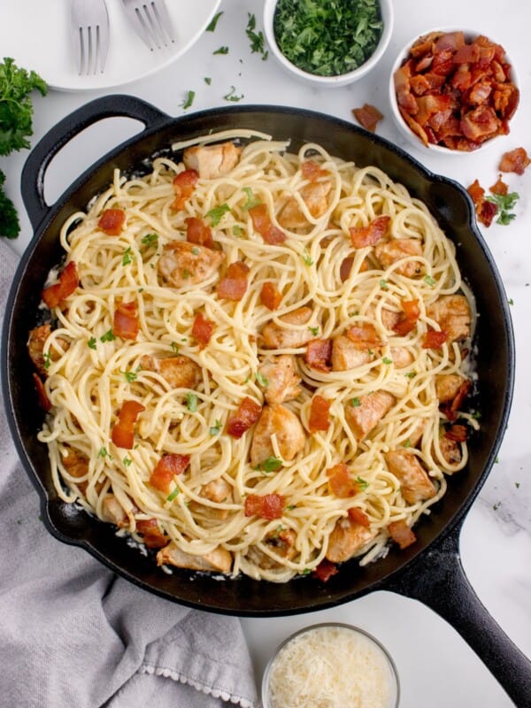 Cast iron pan of chicken carbonara. Pan is surrounded by small bowls of chopped bacon, parmesan, and parsley.