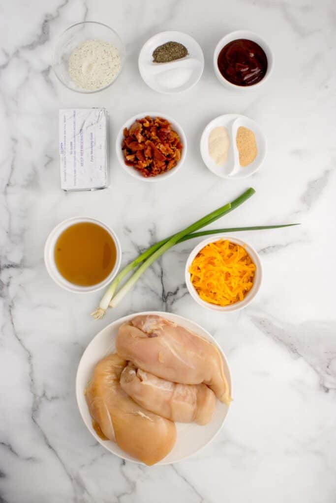 Ingredients for crack chicken recipe: chicken breast, barbecue sauce, bacon, salt, black pepper, onion powder, garlic powder, ranch seasoning mix, chicken stock, cream cheese, sharp cheddar cheese, and sliced green onions.