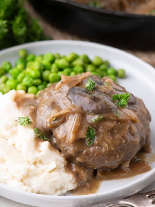 White dinner plate with hamburger steak. Served with mashed potatoes and peas.