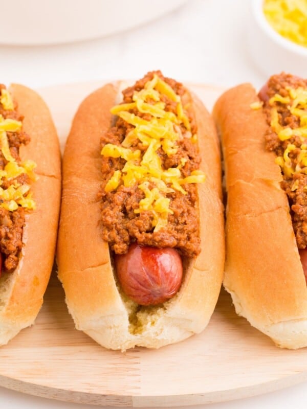 Close up view of a row of hot dogs on a serving platter with homemade chili and shredded cheddar cheese on top.