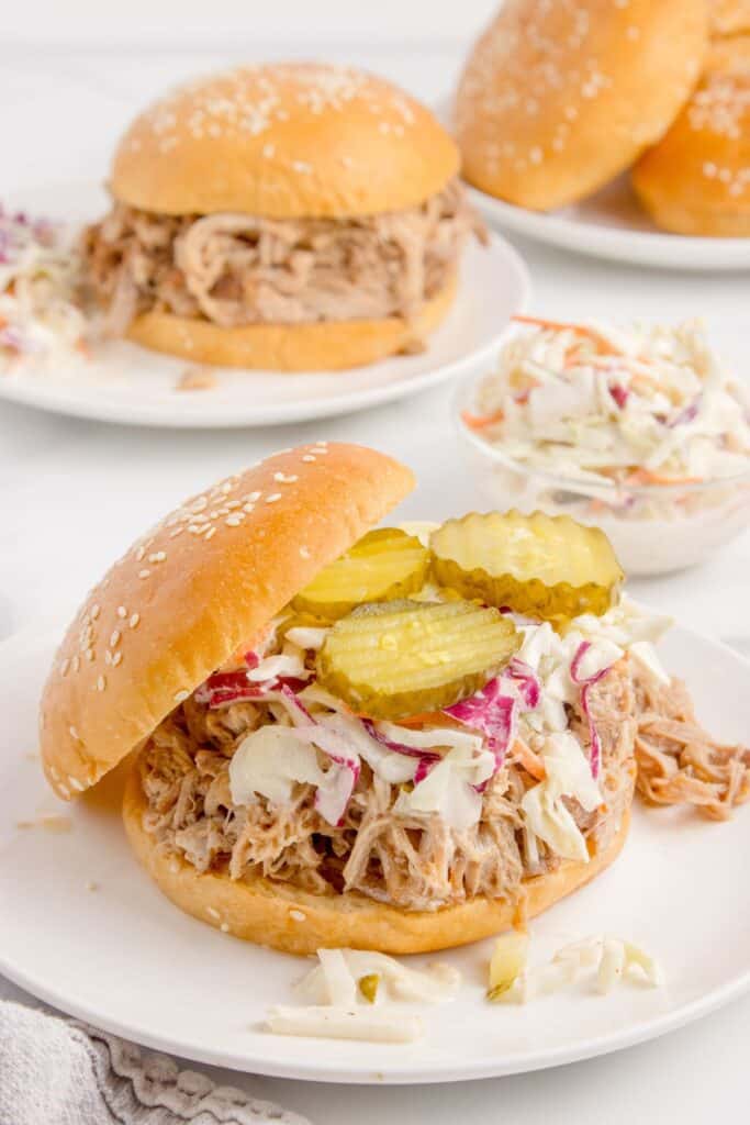 Pork sandwich shown open face. It is layered with pulled pork, coleslaw, and pickles.