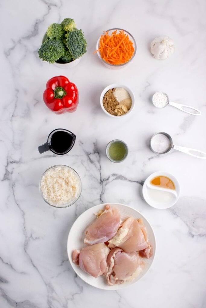 Ingredients for a Teriyaki bowl: chicken thighs, soy sauce, olive oil, rice vinegar, sesame oil, brown sugar, broccoli, carrots, red bell peppers, garlic powder, onion powder, ground ginger, cornstarch, white rice, sesame seeds, and green onions.
