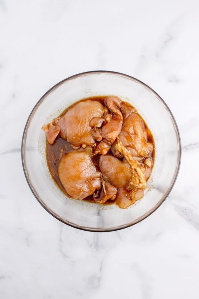 Glass bowl with marinating chicken thighs.