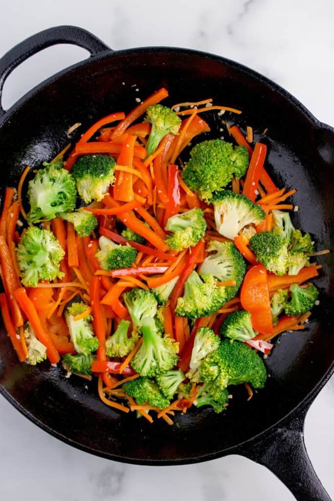 Cast iron pan with chopped veggies, including: red bell pepper, carrots, and broccoli.