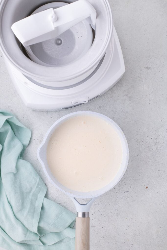 Ice cream base in a sauce pot next to a prepped and frozen ice cream maker.