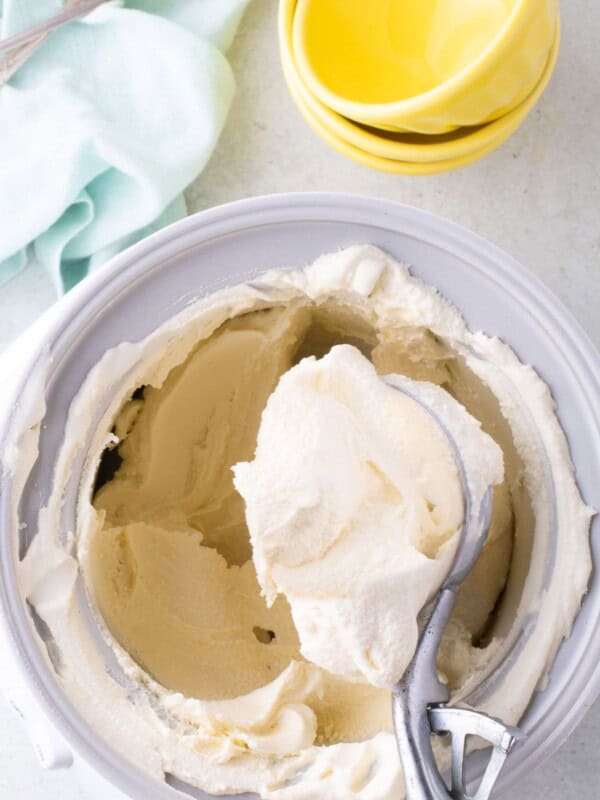 Ice cream insert bowl with homemade vanilla ice cream in it. Old fashioned scoop is lifting a serving out of the insert.