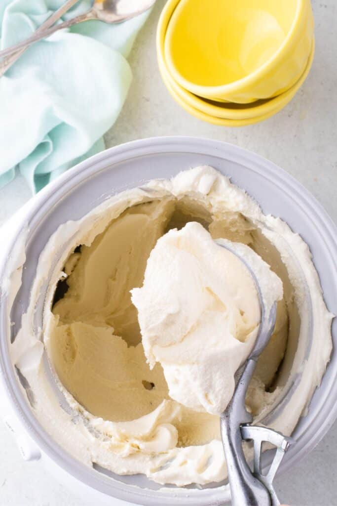 Ice cream insert bowl with homemade vanilla ice cream in it. Old fashioned scoop is lifting a serving out of the insert.