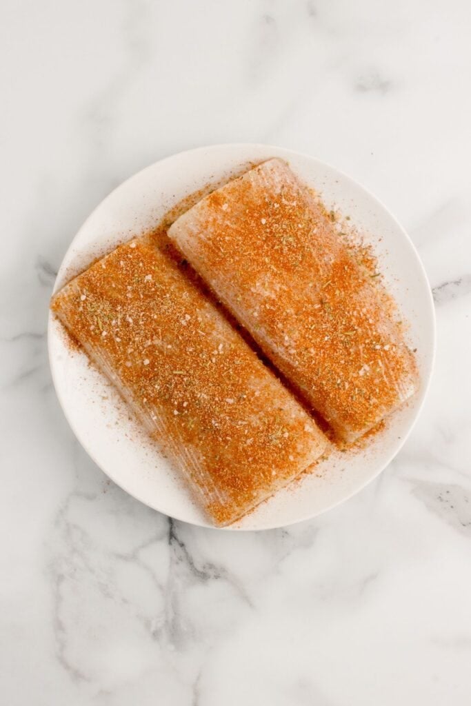Two raw, seasoned mahi mahi fillets on a white plate.