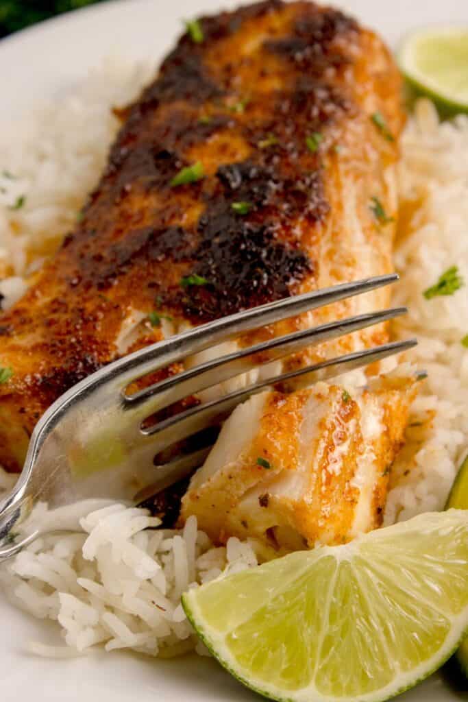 A fork is cutting a bite of tender mahi mahi.