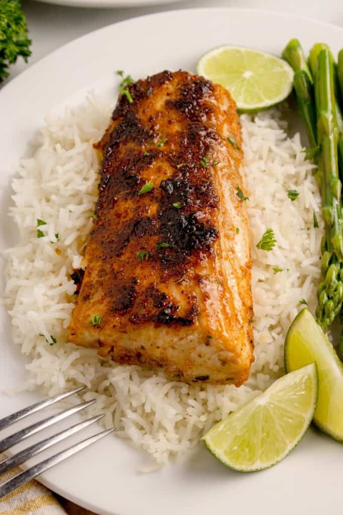 Mahi mahi fillet on a white dinner plate, served over a bed of white rice.