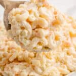 Creamy macaroni salad in a serving bowl with a wooden serving spoon lifting a portion above the bowl.