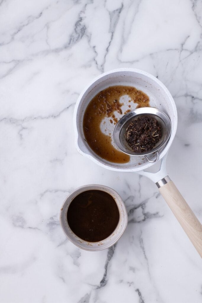 Small saucepan with a strainer in it. A bowl of strained marinade is next to it.
