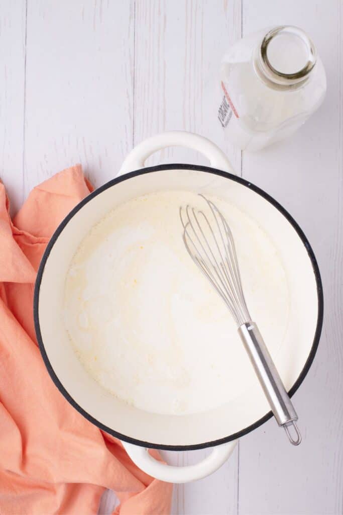 A large white dutch oven with a whisk and a mixture of milk, sugar, and eggs.