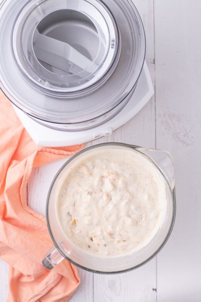 The ice cream base is in a large measuring cup next to an ice cream maker.
