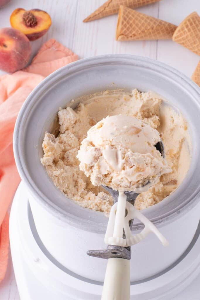Ice cream maker with churned ice cream in it. An ice cream scoop is lifting a serving above the bowl.