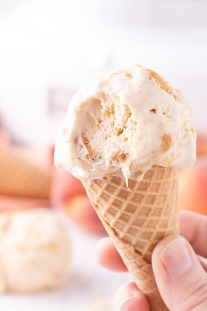 A scoop of peach ice cream on a sugar cone with a bite taken out of it.