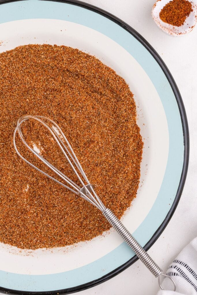 Chicken taco seasoning on a blue and white plate with a whisk.