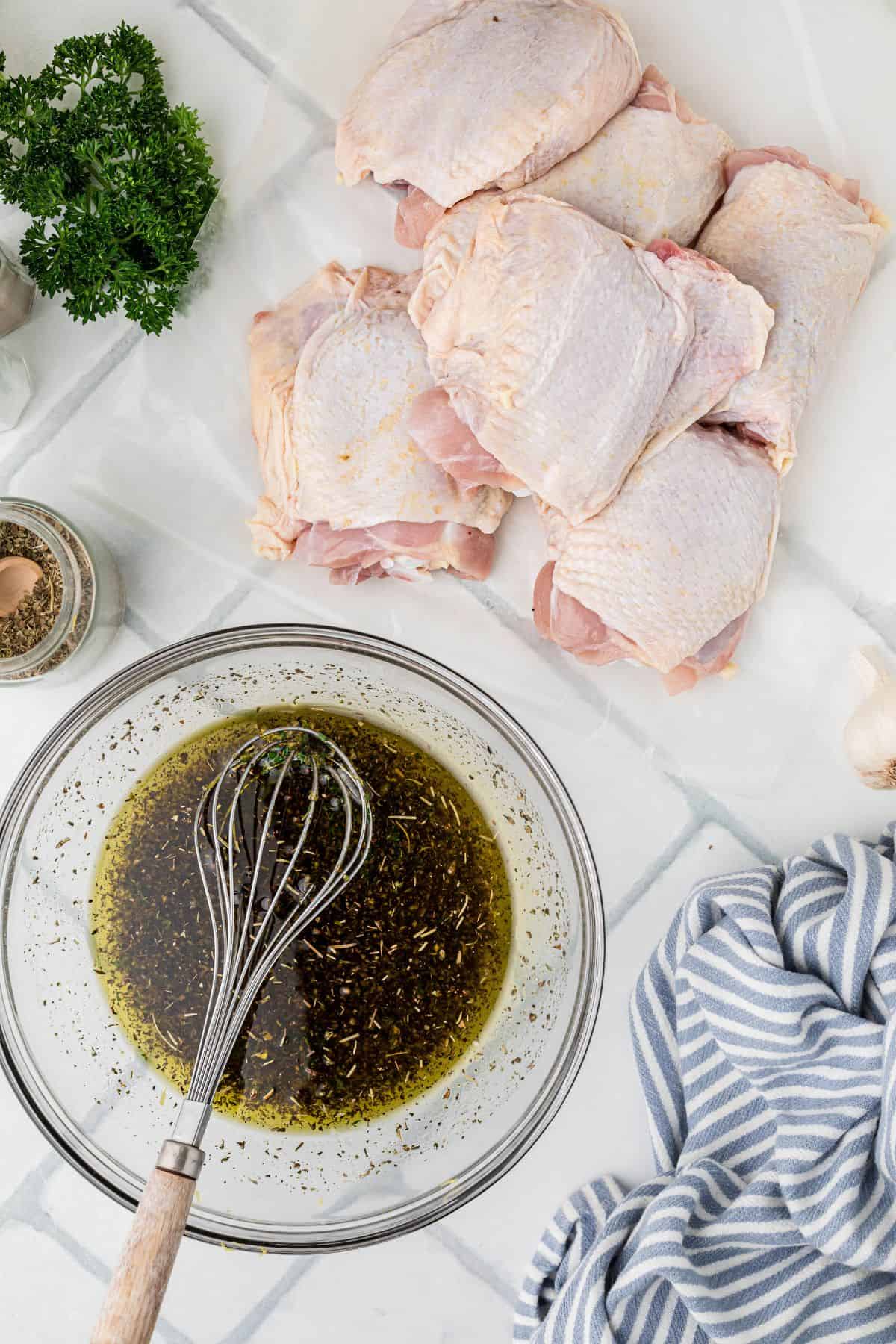 Marinade for chicken in a glass bowl next to a pile of raw chicken thighs.