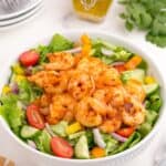 Completed shrimp salad in a white serving bowl. A glass jar holds the homemade dressing.
