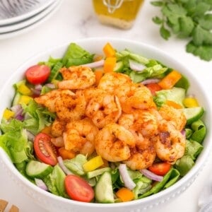 Completed shrimp salad in a white serving bowl. A glass jar holds the homemade dressing.