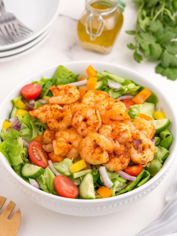 Completed shrimp salad in a white serving bowl. A glass jar holds the homemade dressing.