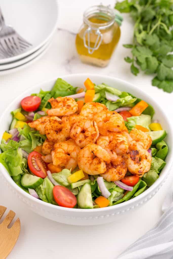 Completed shrimp salad in a white serving bowl. A glass jar holds the homemade dressing.