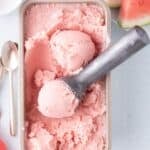 Large pan of watermelon ice cream. A scoop of ice cream is in the ice cream scoop.