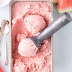 Large pan of watermelon ice cream. A scoop of ice cream is in the ice cream scoop.