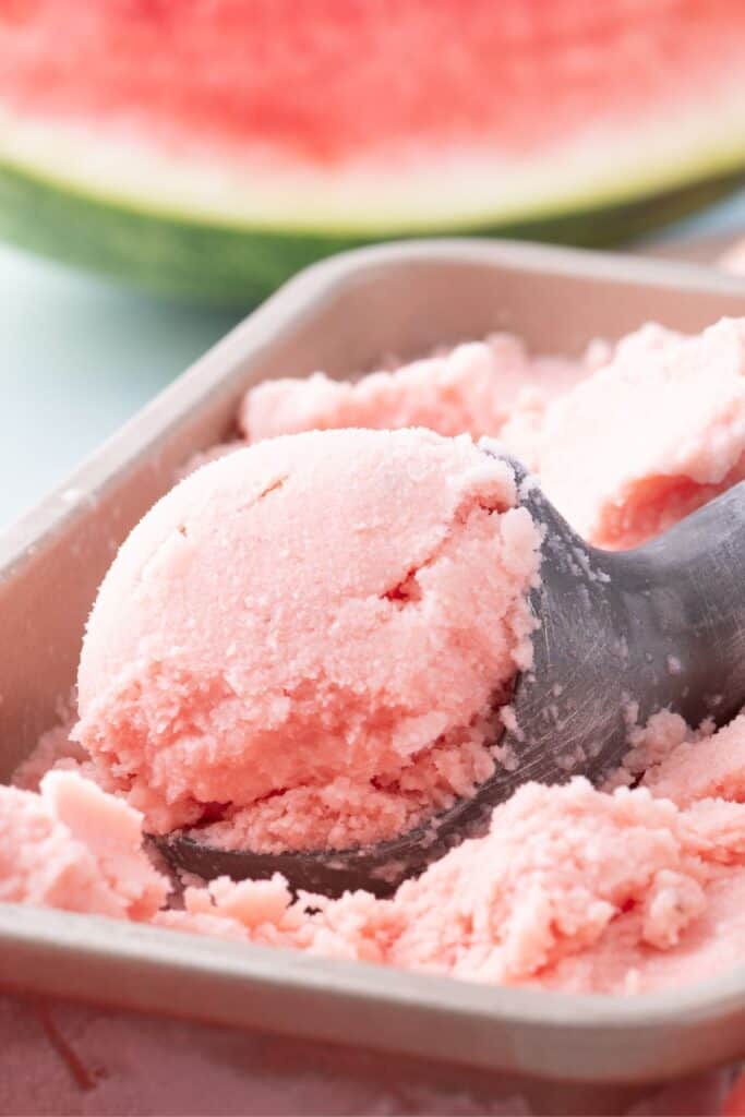 Up close image of watermelon ice cream in an ice cream scoop.