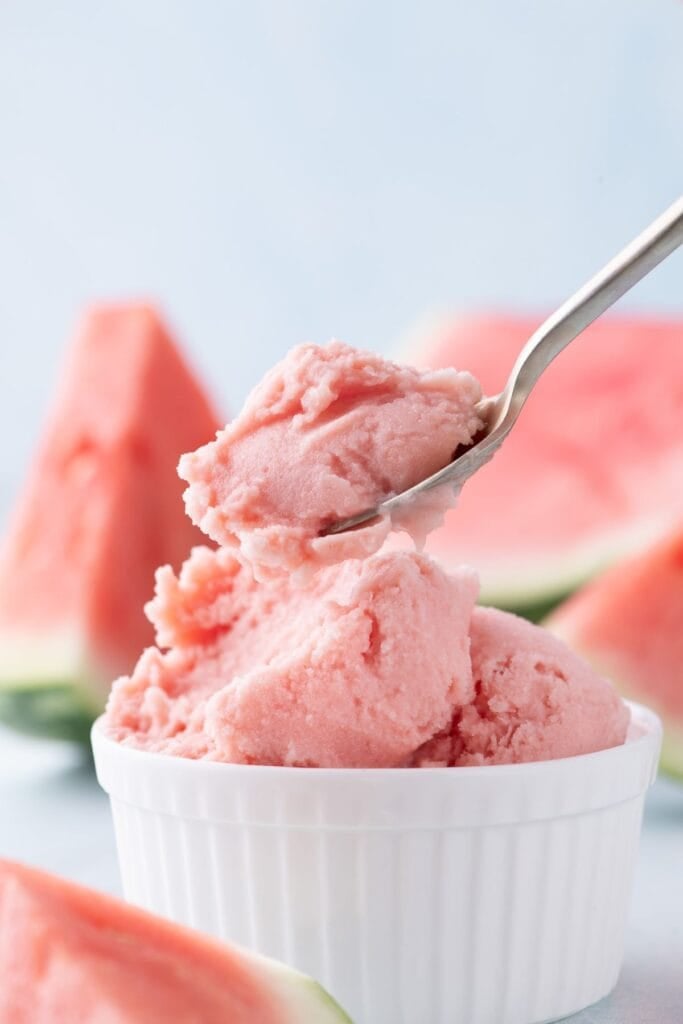 A small white bowl of watermelon ice cream with a spoon lifting a bite up.