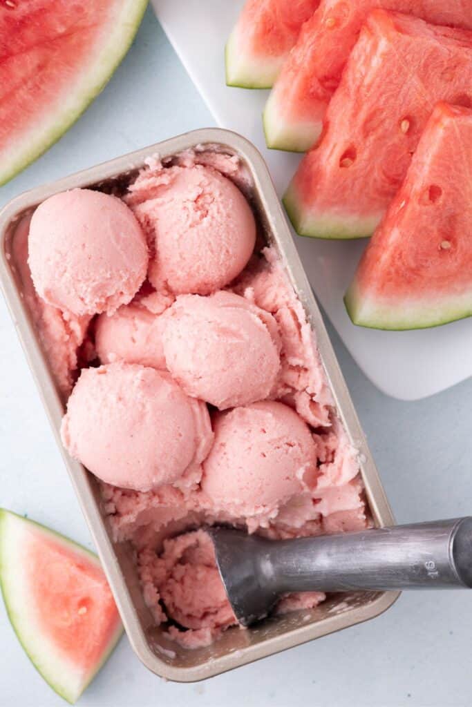 A large pan full of watermelon ice cream. The pan is surrounded by sliced watermelon.
