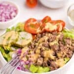 Burger bowl with burger sauce drizzled on top. Bowl is surrounded by small bowls of halved tomatoes and chopped purple onion.