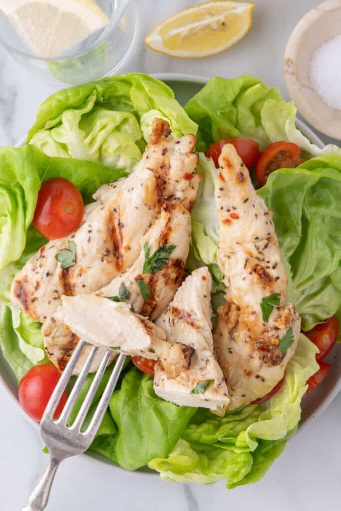 Chicken tenders over a plate of salad greens and tomatoes.