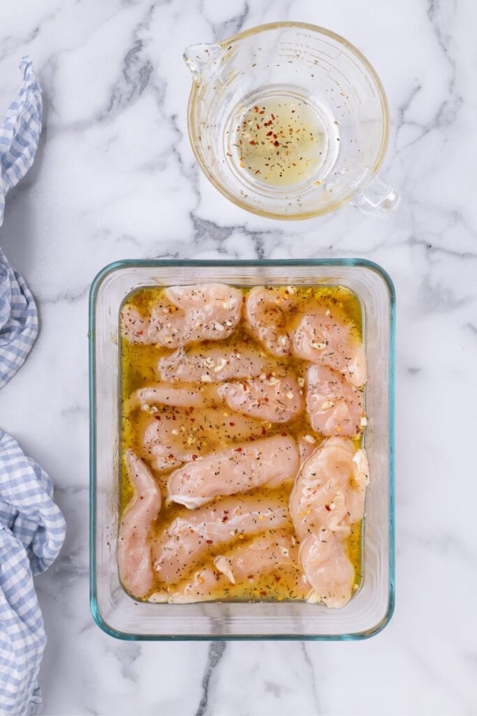Chicken tenders marinating in a glass container.