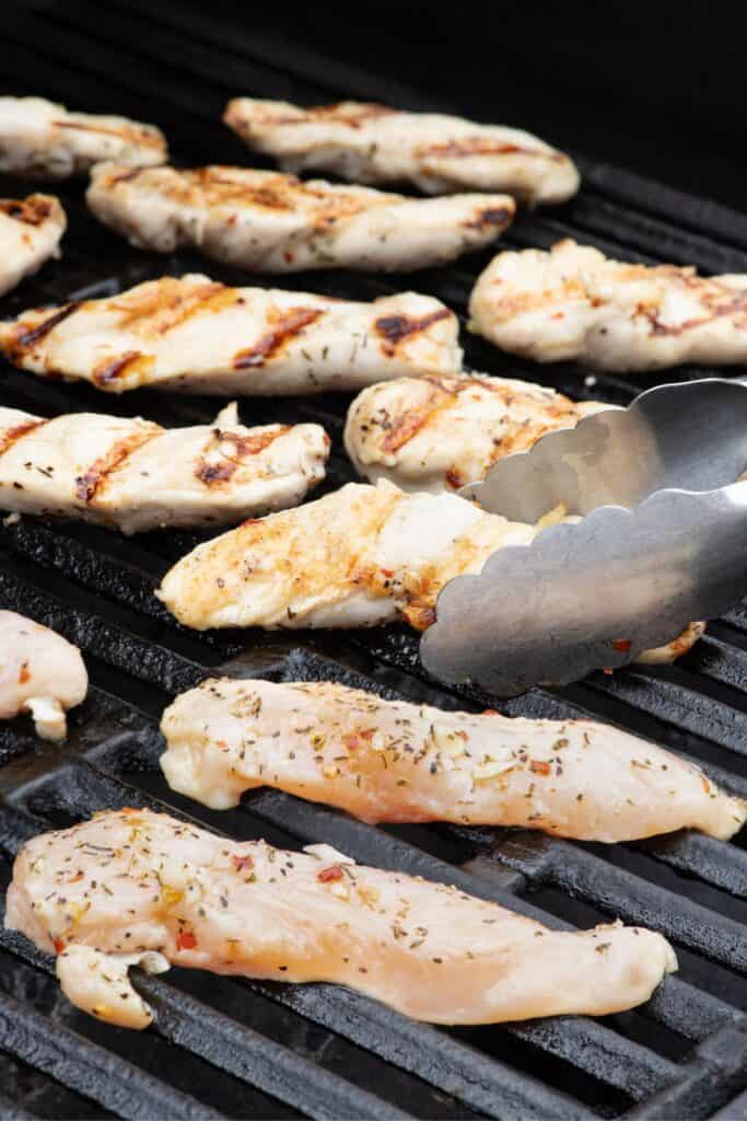 Chicken tenders cooking on grill grates.