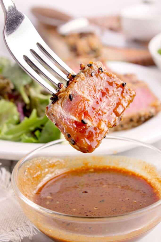 A bite of tuna steak on a fork being dipped in a sauce.