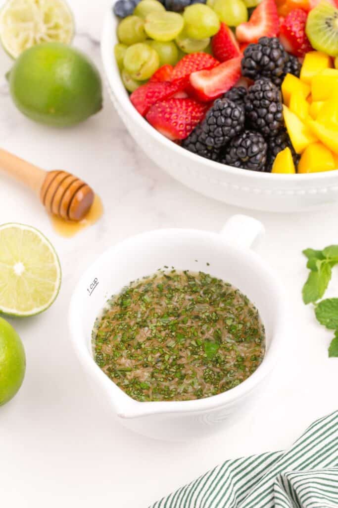 Closeup of the fruit salad dressing in a bowl with fresh fruit in the background.